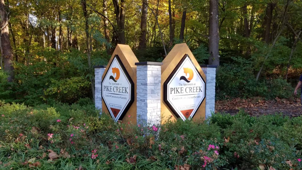 Monument sign for apartment community with two internally illuminated light boxes mounted between three faux stone columns.